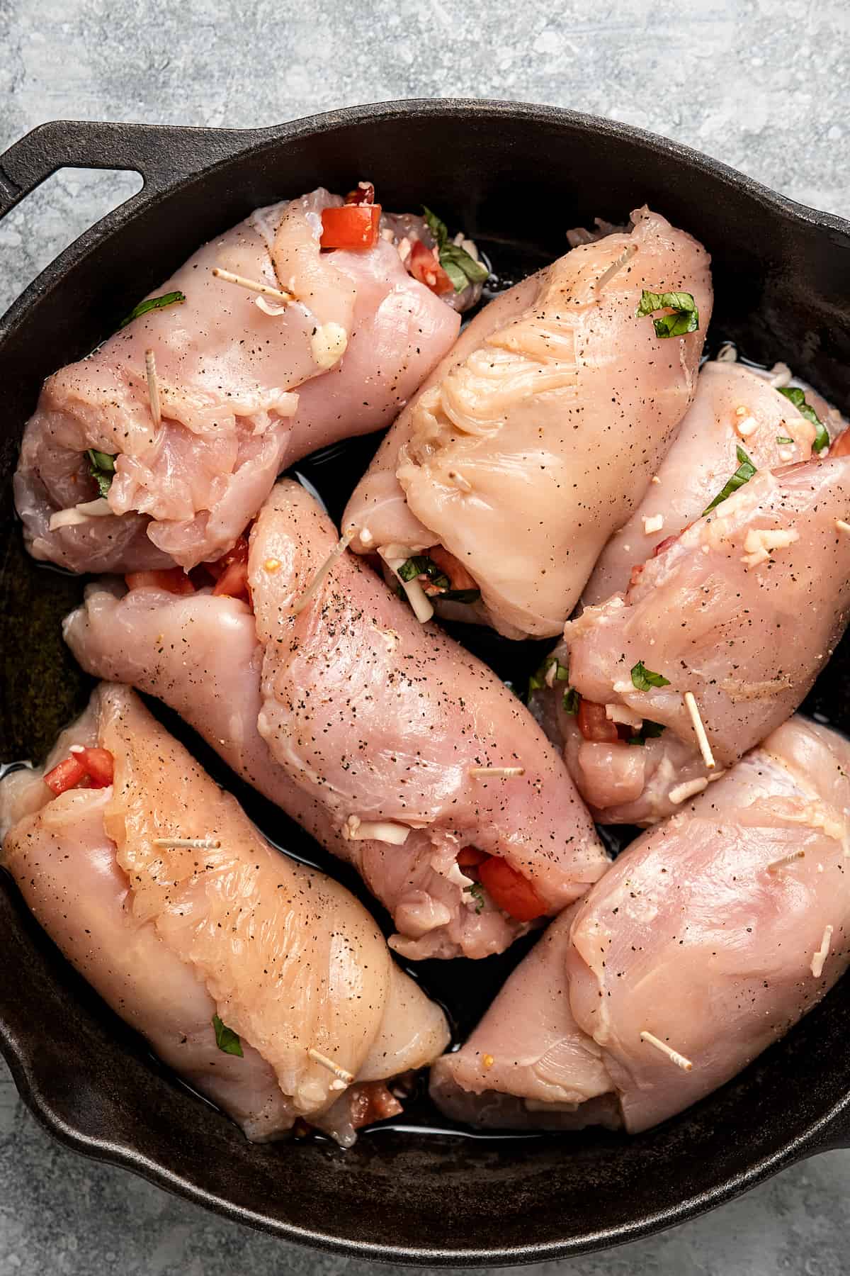Uncooked bruschetta stuffed chicken breasts in a skillet.