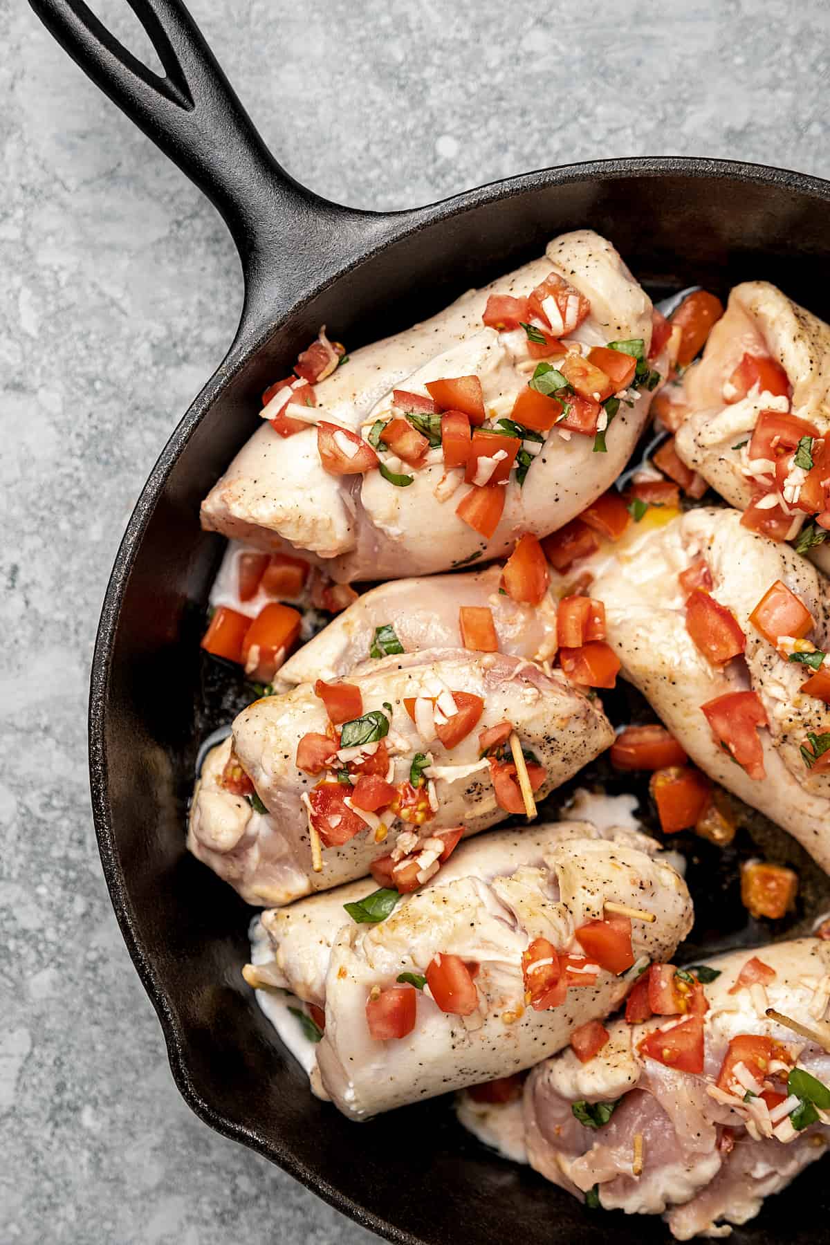 Uncooked bruschetta stuffed chicken breasts in a skillet topped with additional tomato mixture.