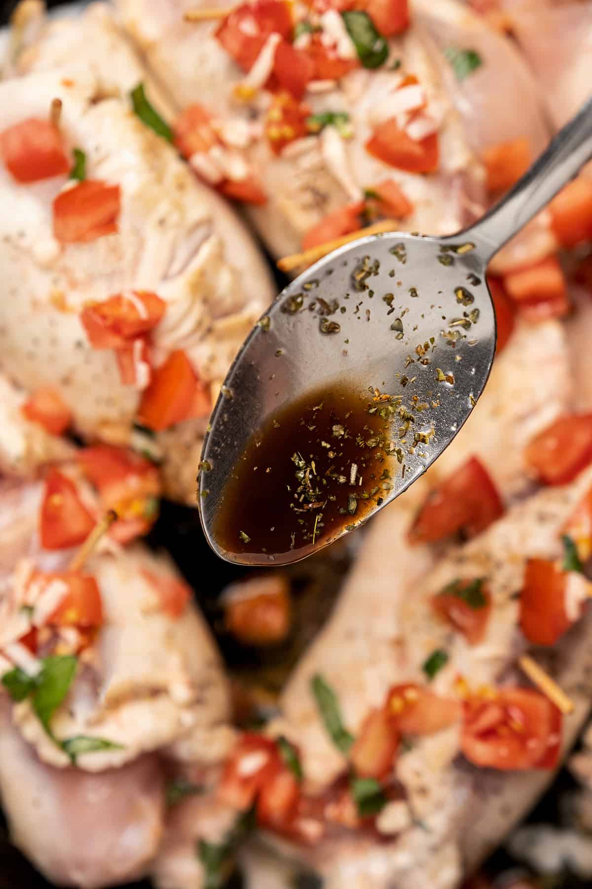 A spoon drizzles balsamic sauce overtop uncooked bruschetta stuffed chicken breasts in a skillet.