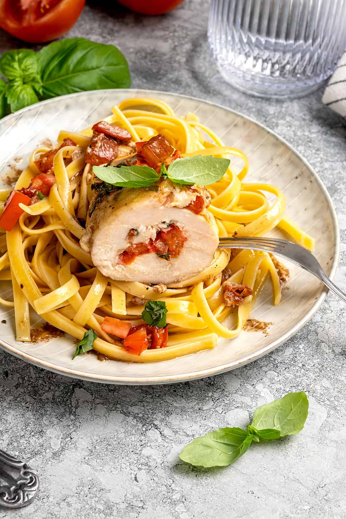 Sliced bruschetta stuffed chicken breast served over a plate of pasta, garnished with basil leaves.