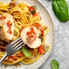 A forkful of bruschetta stuffed chicken on a plate with chicken and pasta.
