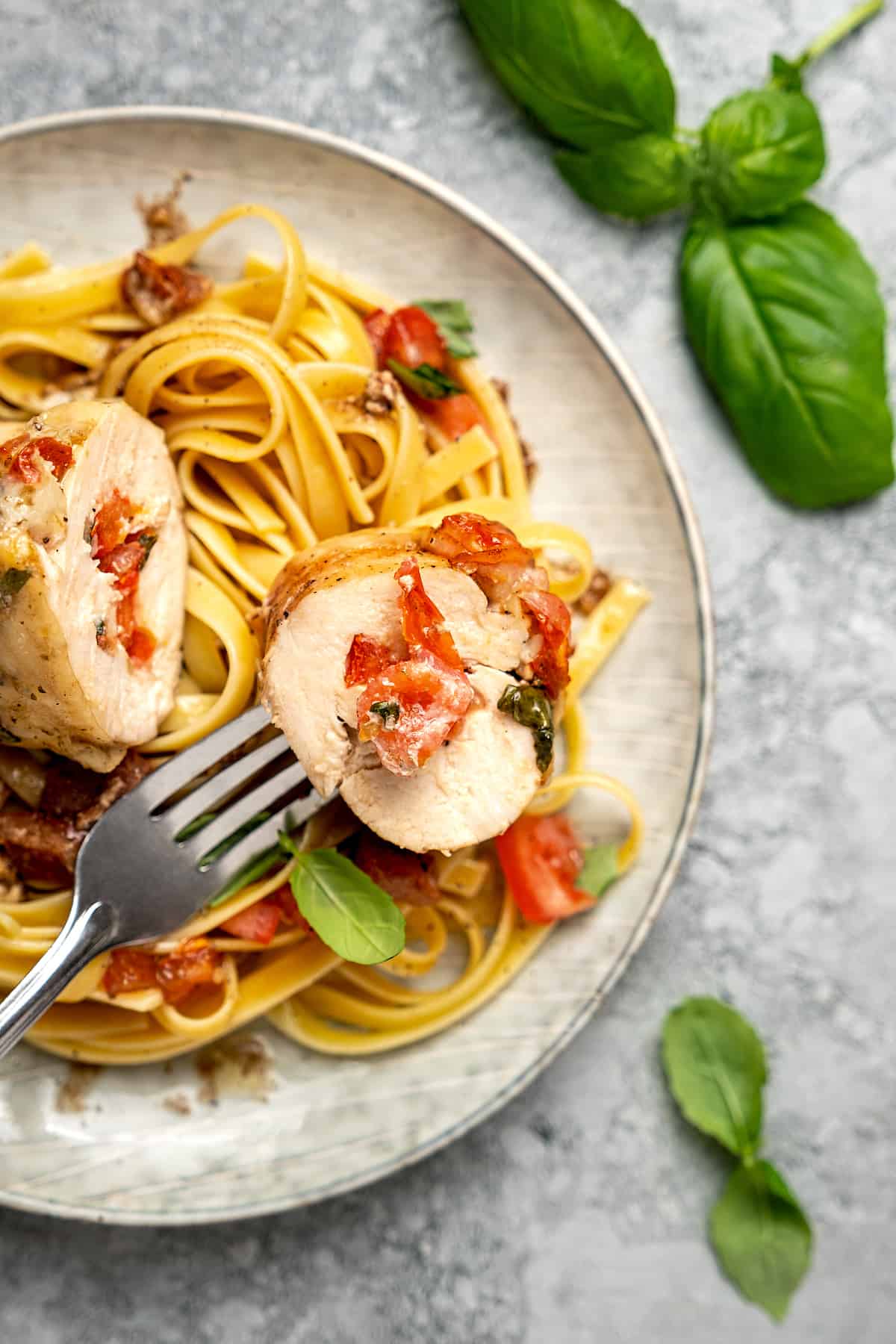 A forkful of bruschetta stuffed chicken on a plate with chicken and pasta.