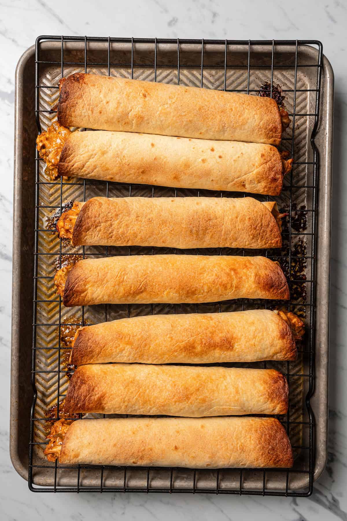 Baked chicken flautas on a wire rack set over a baking sheet.