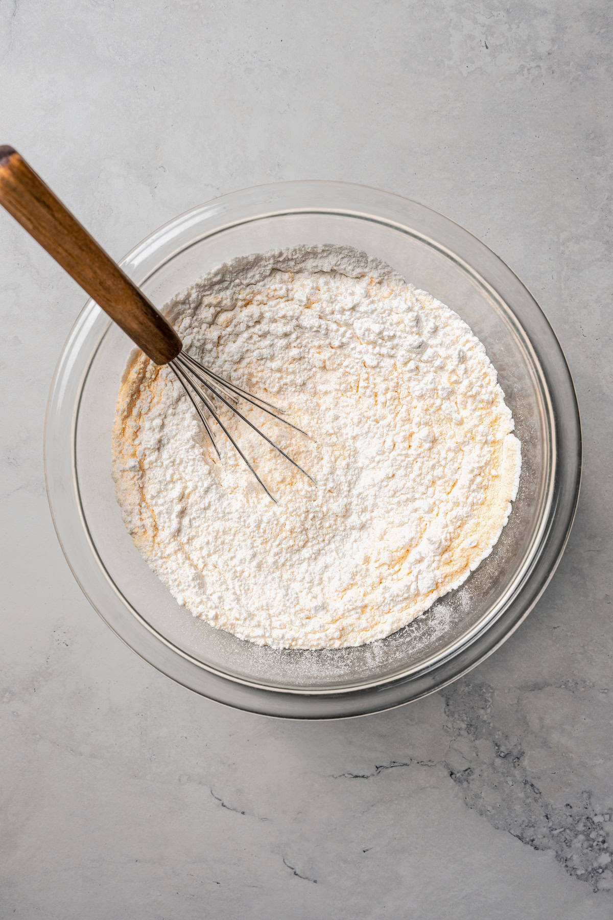 Dry ingredients whisked together in a glass bowl with a wooden-handled whisk.