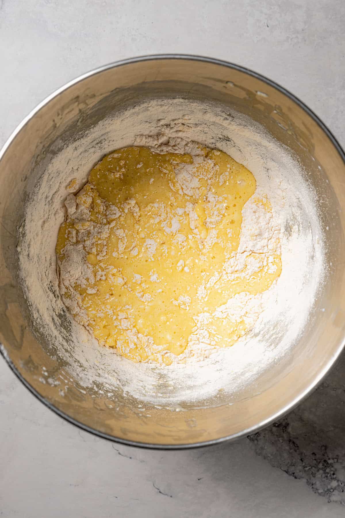 Dry ingredients partially incorporated into the wet cake batter in a metal bowl.