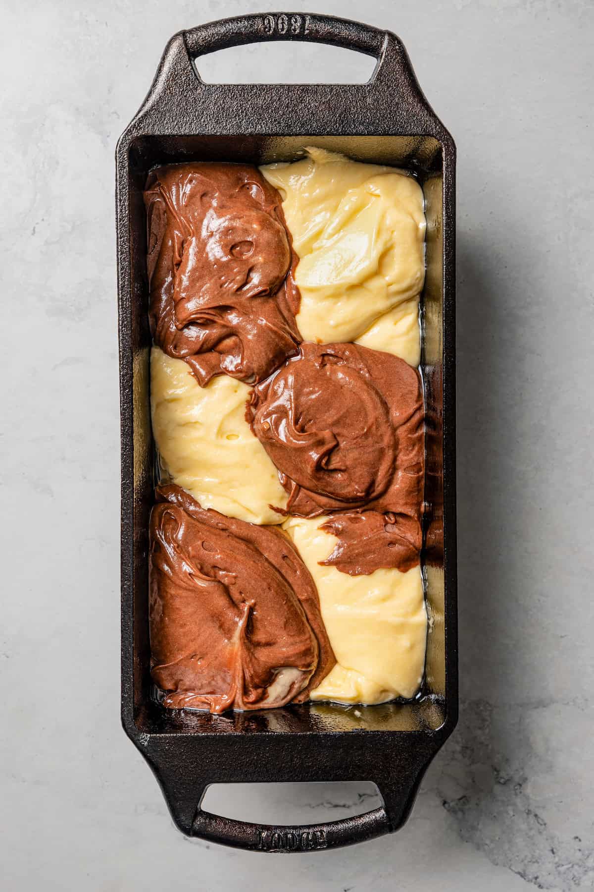 Overhead view of vanilla and chocolate cake batter layered into a metal loaf pan.