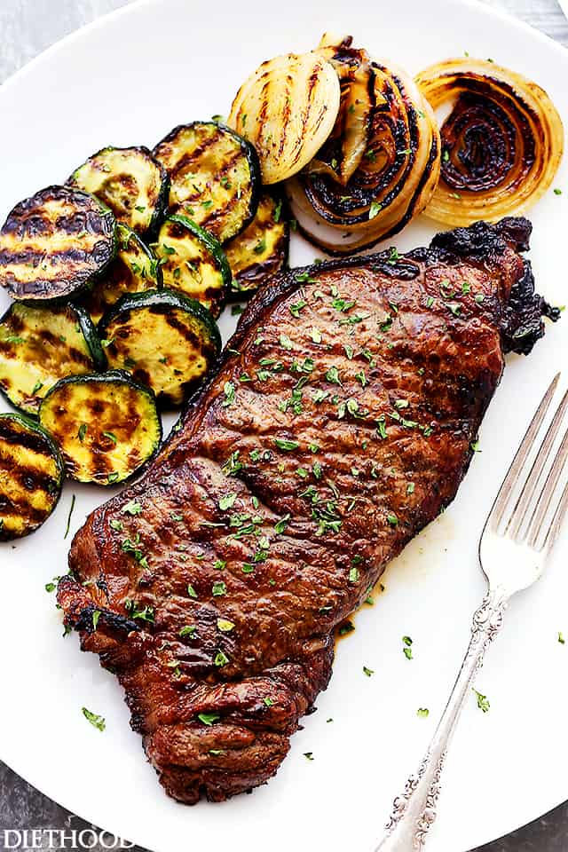 Jack Daniel's grilled steak next to grilled zucchini and onion on a plate, with a fork.