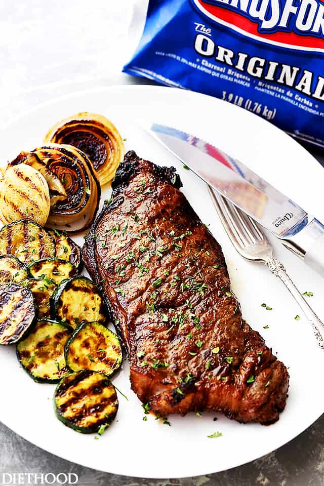 Jack Daniel's grilled steak next to grilled zucchini and onion on a plate, with a fork and knife.