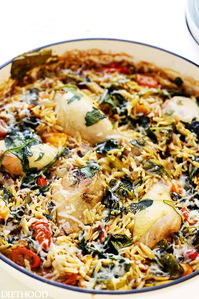 A photo of chicken nestled in a pot of orzo with cooked spinach and tomatoes.