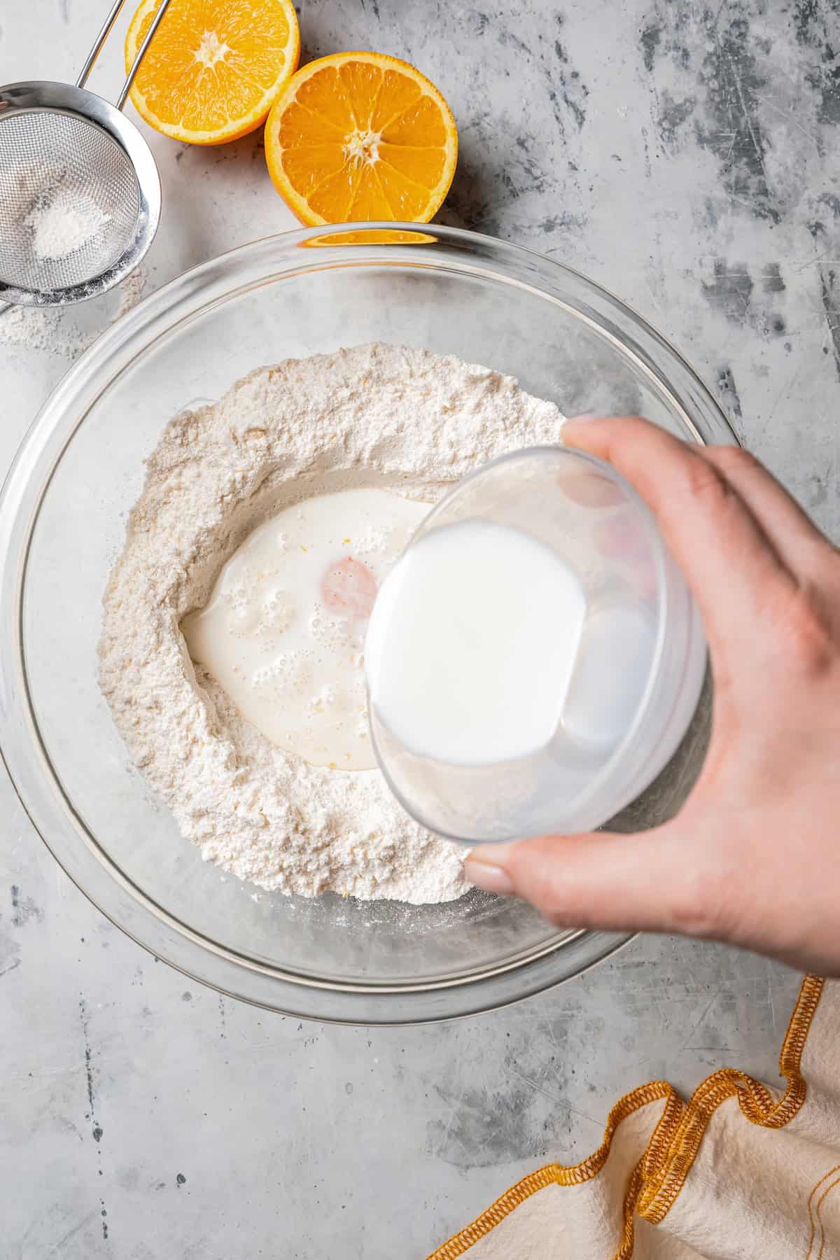 Milk being poured into a well of dry ingredients inside a glass bowl.