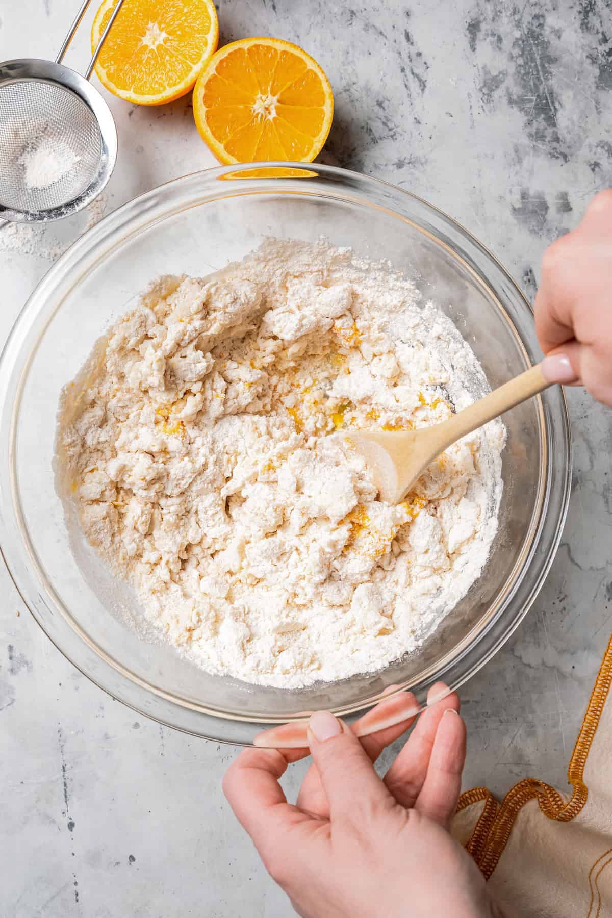 A hand holding a bowl of scone ingredients while the other hand uses a wooden spatula to fold the dough together.