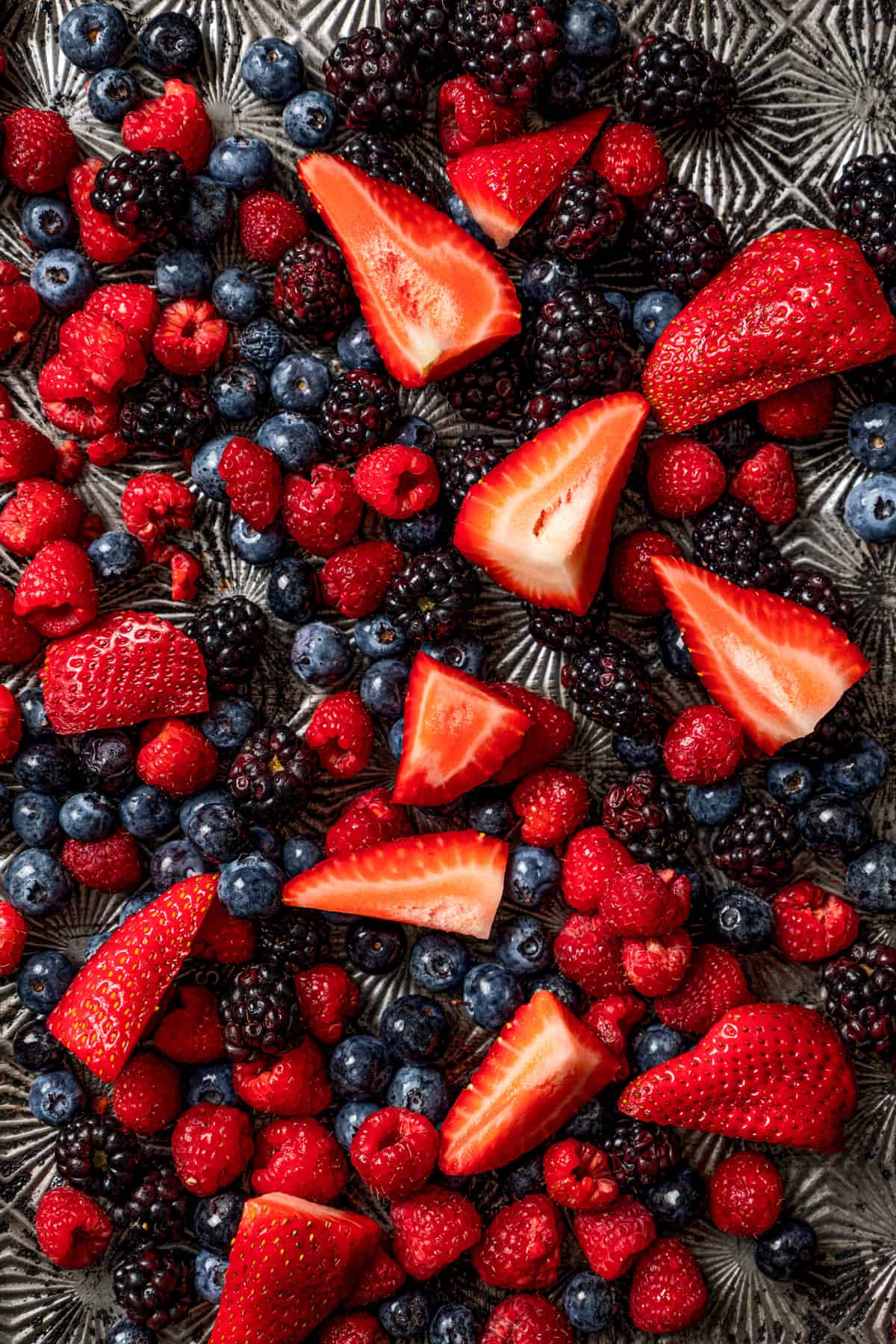 Close-up photo of a bunch of sliced strawberries, blueberries, and raspberries.