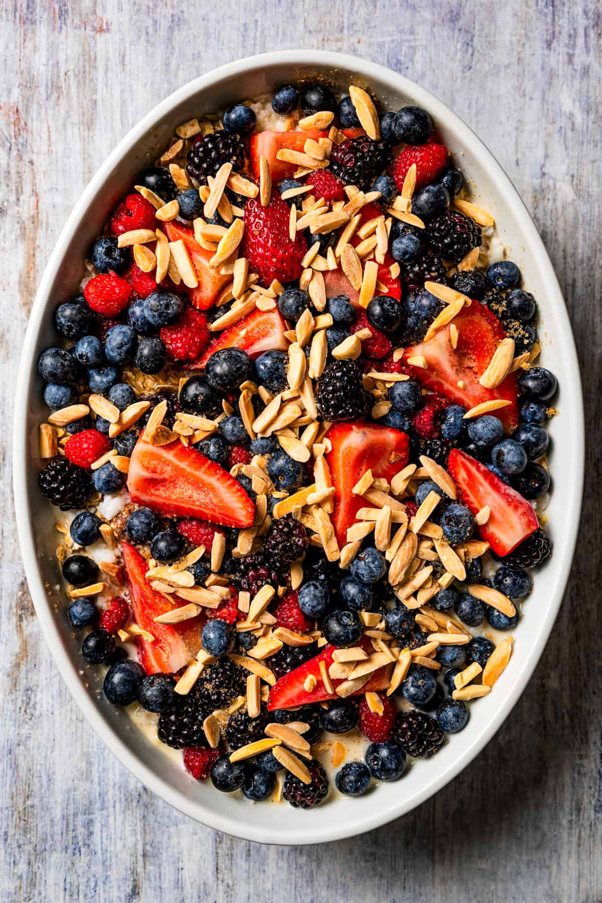 Assembled oatmeal tossed with berries and arranged in an oval casserole dish.