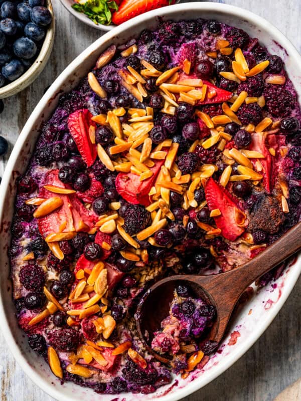 Overhead view of baked berry oatmeal in an oval casserole dish with a wooden spoon.