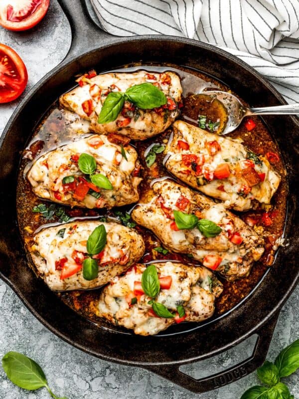 Overhead photo of a skillet with stuffed chicken rollups, garnished with diced tomatoes and fresh basil leaves.