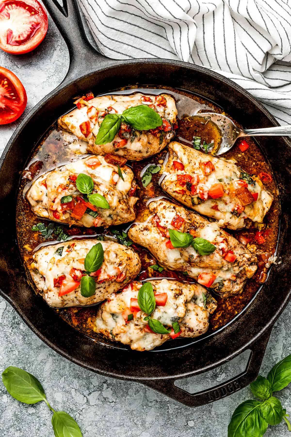 Bruschetta chicken breasts cooking in a skillet with balsamic sauce.