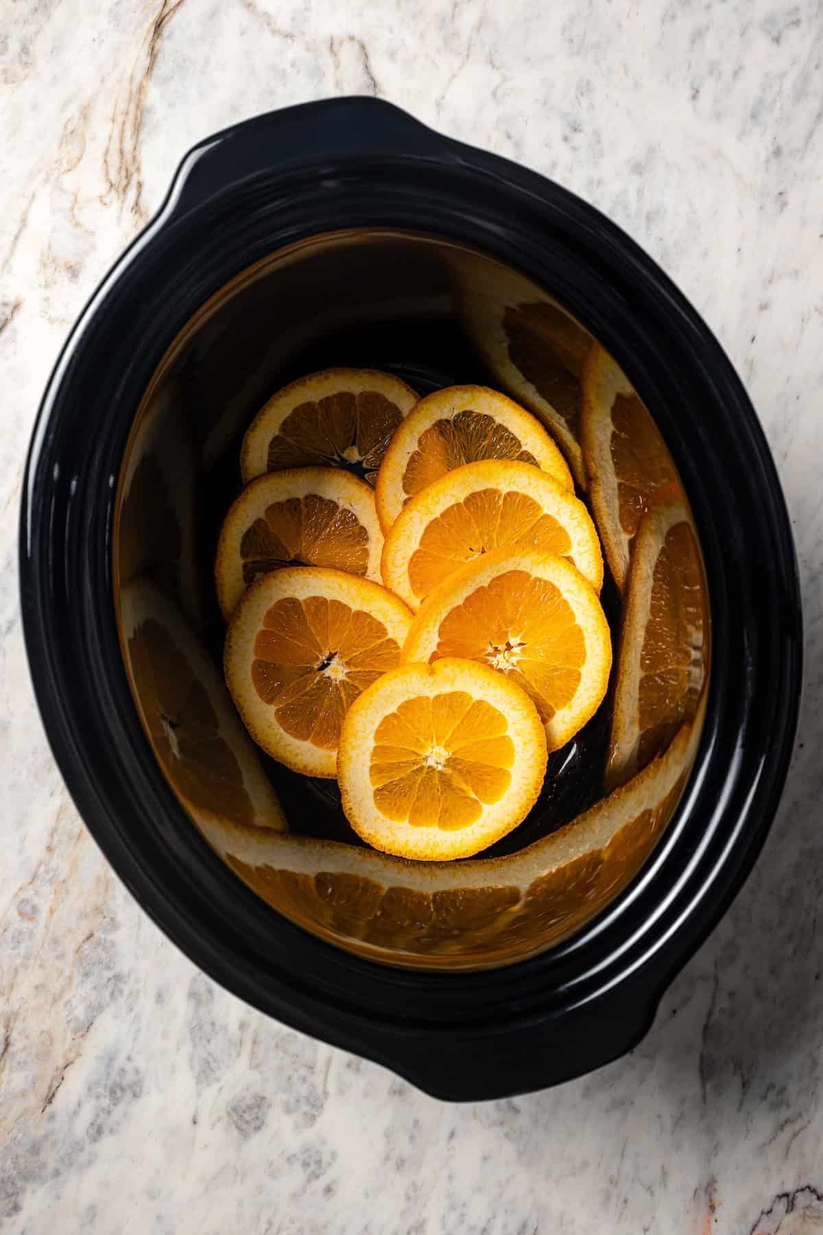 Orange slices arranged in the bottom of a crock pot.