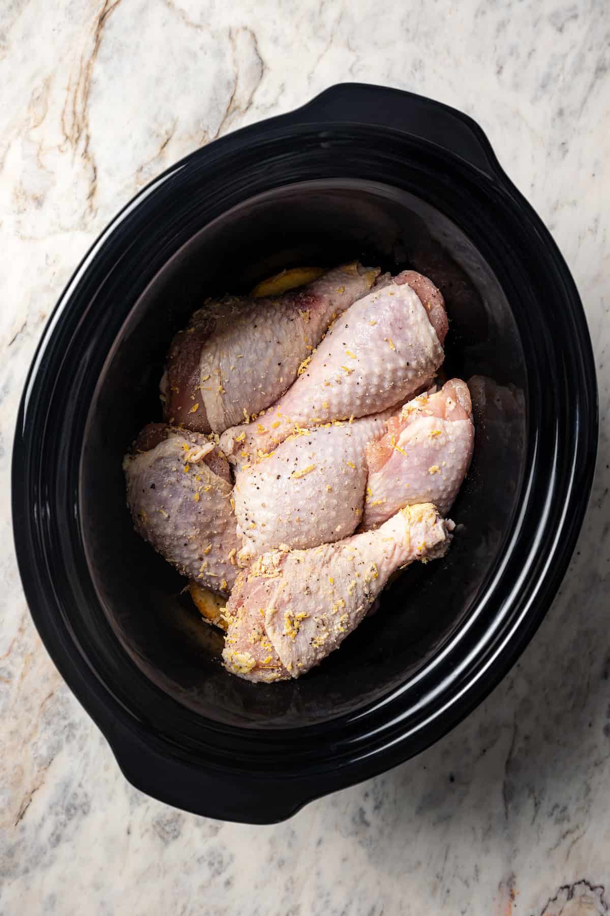 Chicken drumsticks arranged over top of orange slices in a crock pot.