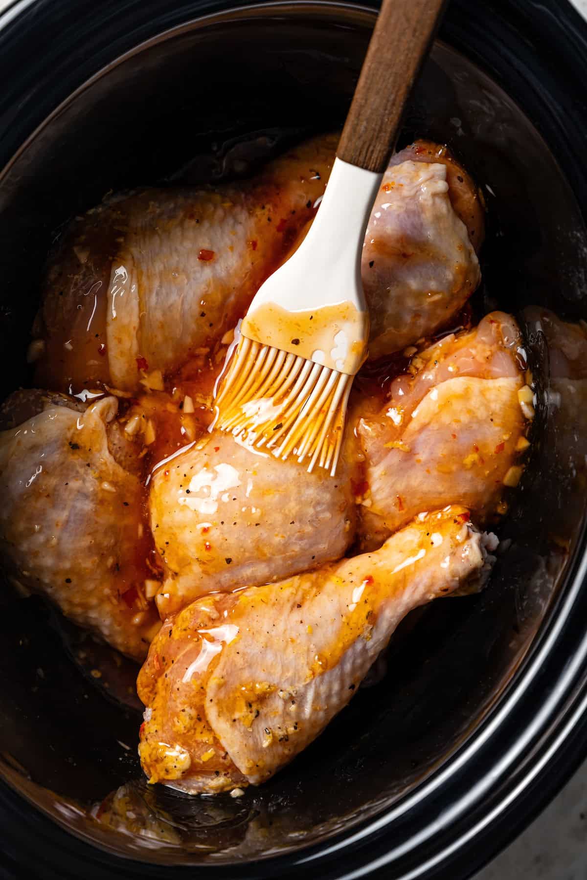 A basting brush is used to brush citrus soy marinade over chicken drumsticks in the crock pot.