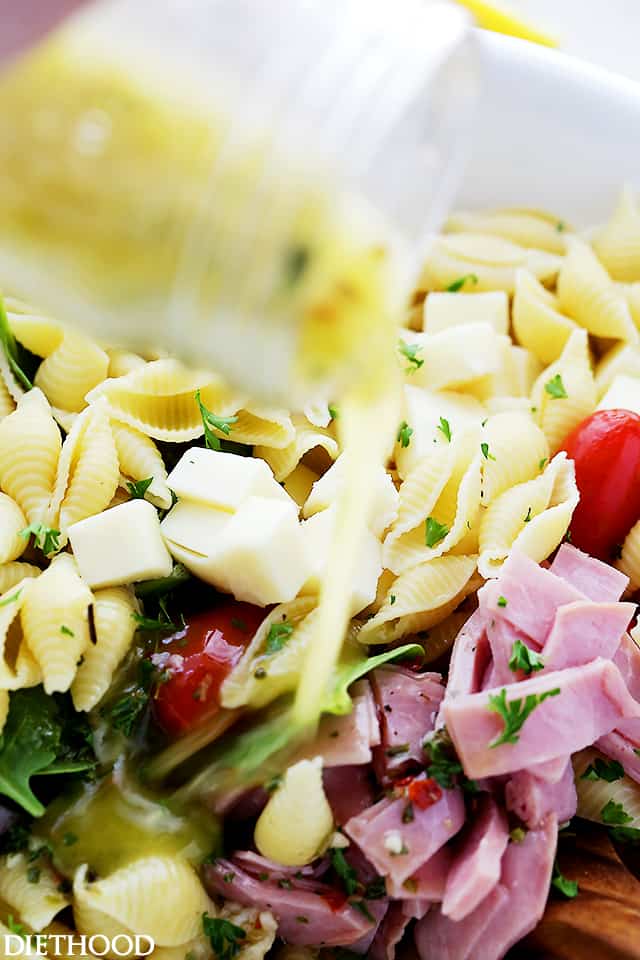 Italian salad dressing is poured over a bowl of Italian pasta salad.