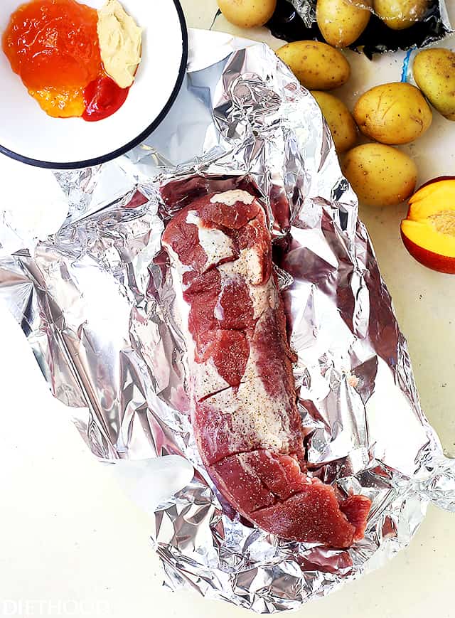 A raw tenderloin with slits cut into it on top of a sheet of foil