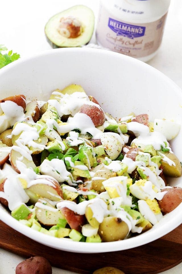 Red potato salad drizzled with creamy dressing in a large white bowl.