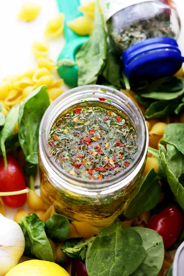 A jar filled with a homemade dressing made with olive oil, vinegar, garlic, and dried herbs.