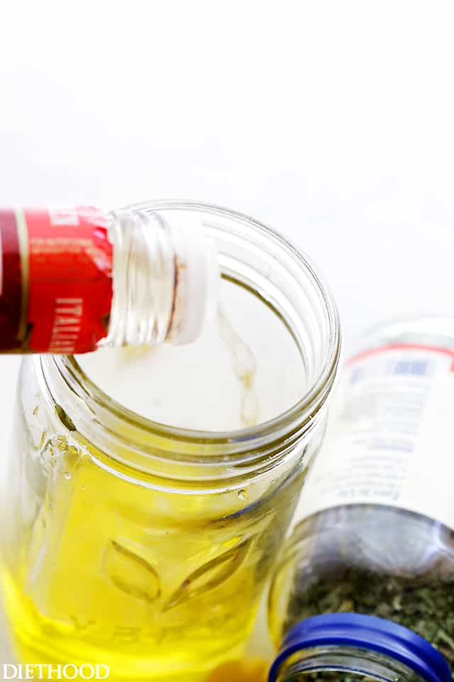 Pouring white wine vinegar into olive oil in a jar.