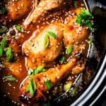 Crock pot chicken drumsticks garnished with sesame seeds and green onions inside the slow cooker.