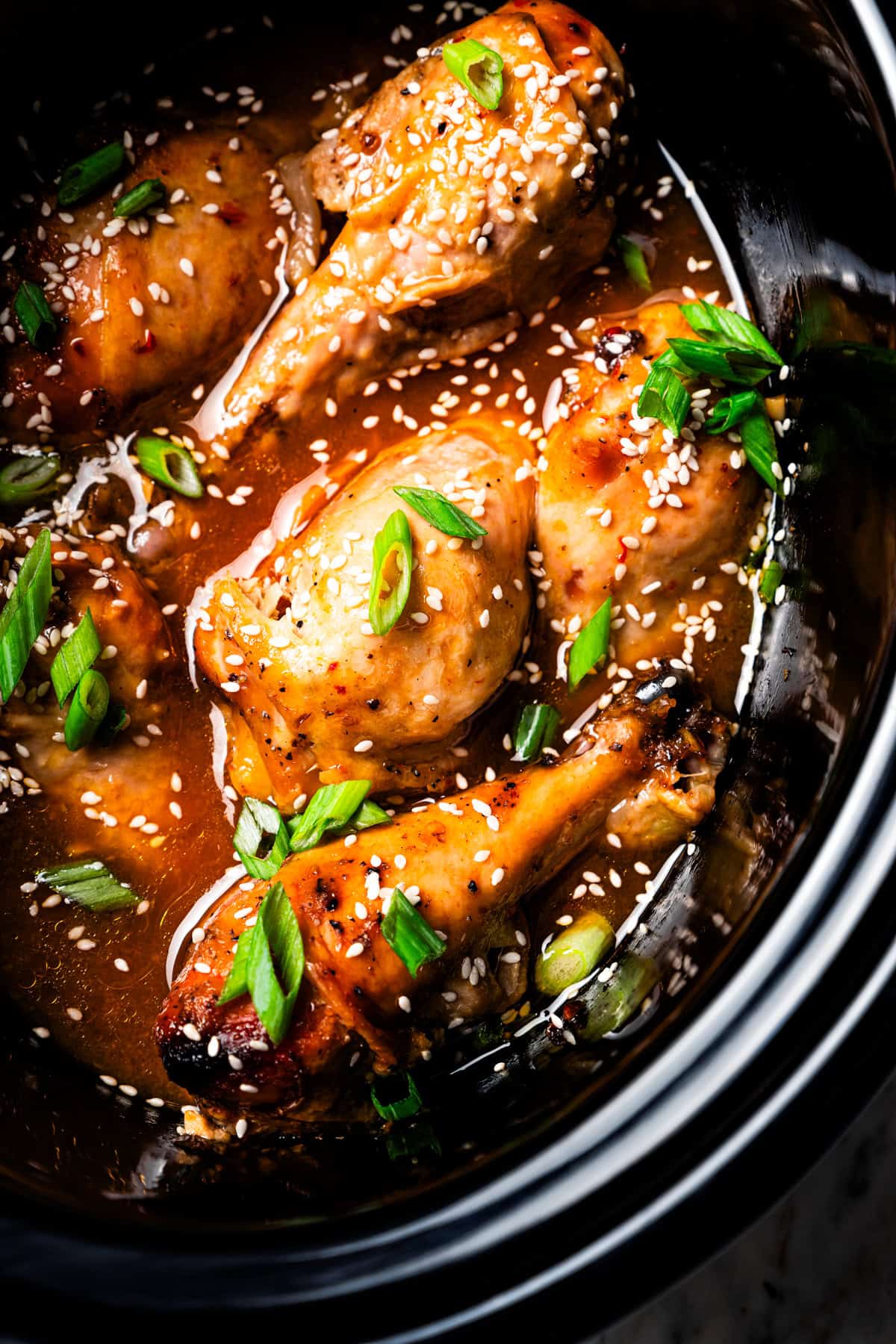 Crock pot chicken drumsticks garnished with sesame seeds and green onions inside the slow cooker.