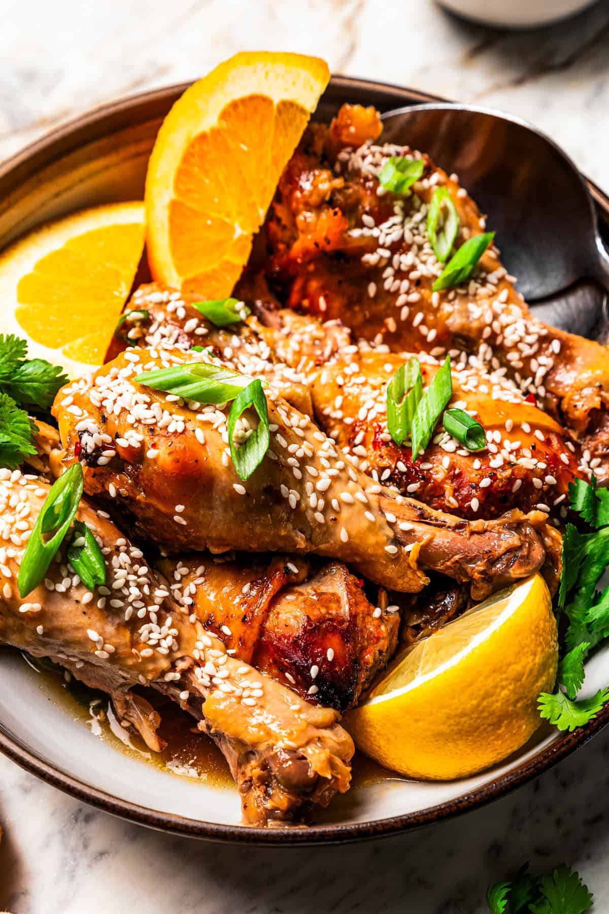 Crockpot chicken drumsticks garnished with sesame seeds, orange wedges, and green onions on a dinner plate.