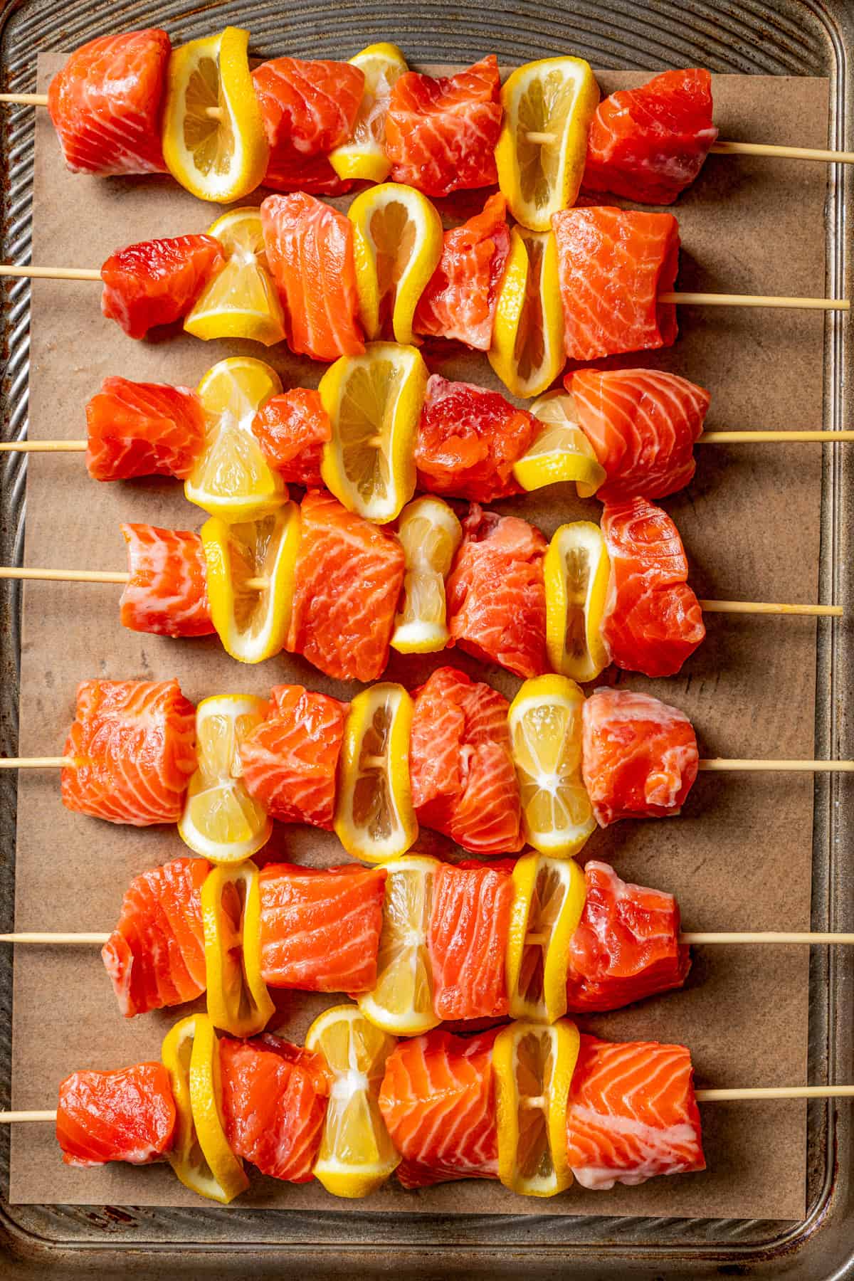 These juicy salmon kabobs with lemon are perfect for grilling! Serve with garlicky yogurt dipping sauce for a delicious and easy summer meal. Assembled salmon kabobs on skewers arranged on a baking sheet.