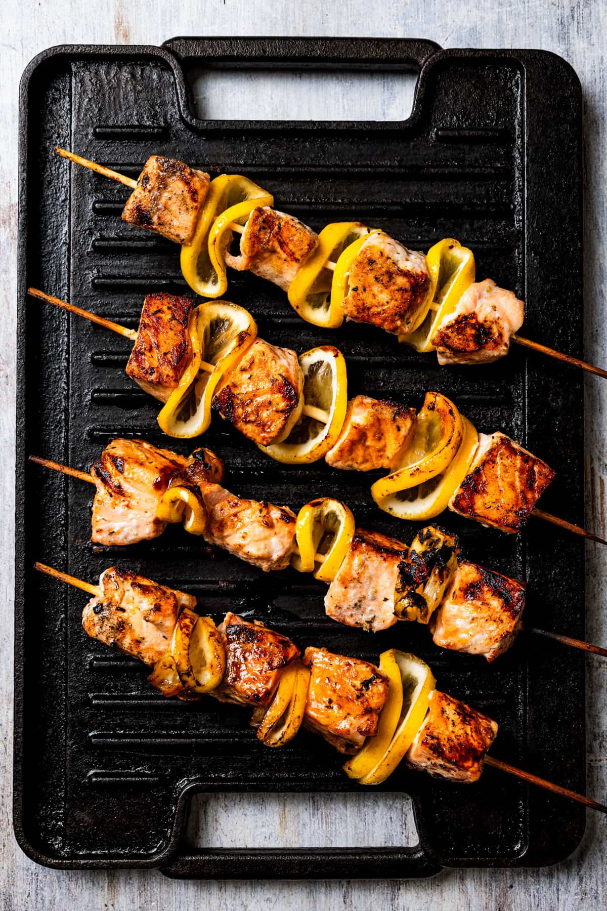 These juicy salmon kabobs with lemon are perfect for grilling! Serve with garlicky yogurt dipping sauce for a delicious and easy summer meal. Salmon skewers are arranged on a grill.