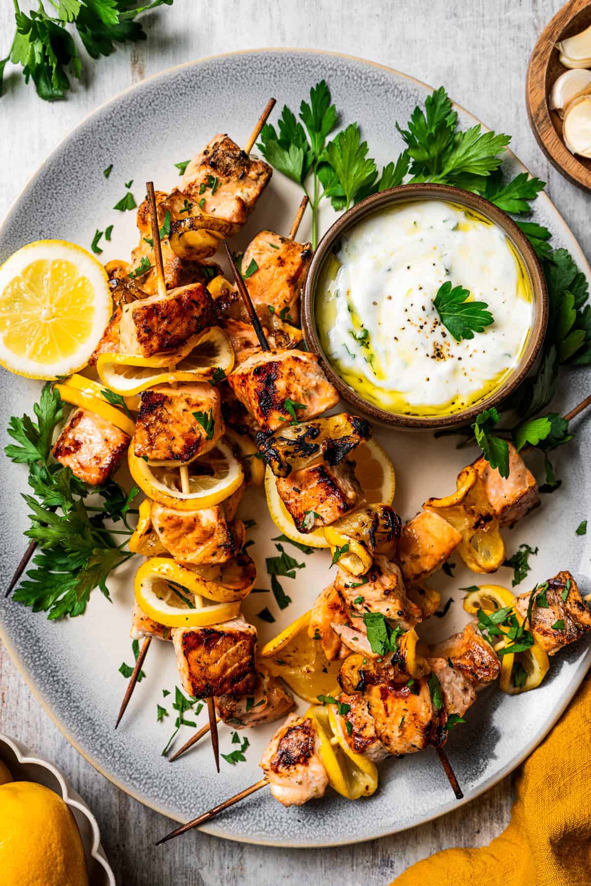 These juicy salmon kabobs with lemon are perfect for grilling! Serve with garlicky yogurt dipping sauce for a delicious and easy summer meal. Salmon kabobs are served next to a bowl of garlic sauce on a white platter.