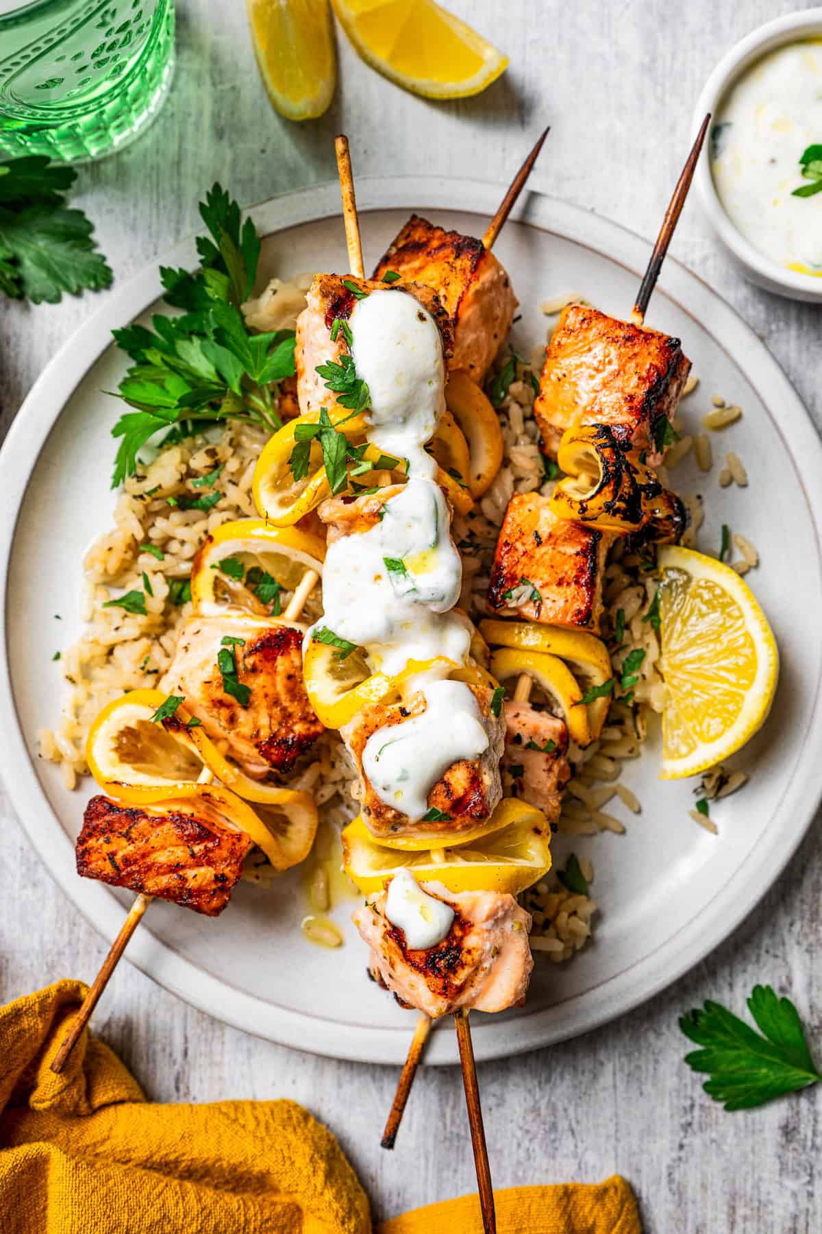 These juicy salmon kabobs with lemon are perfect for grilling! Serve with garlicky yogurt dipping sauce for a delicious and easy summer meal. Salmon skewers served over a bed of rice on a plate, topped with garlic sauce and garnished with lemon wedges.