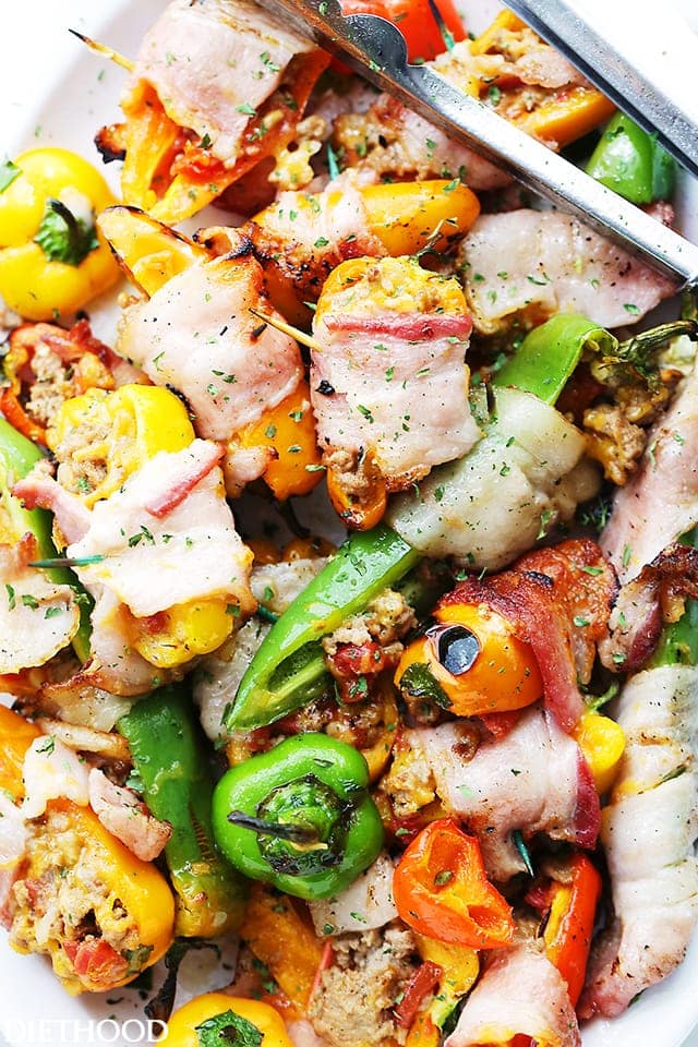 Close up overhead view of grilled stuffed mini peppers on a platter with a set of grilling tongs.