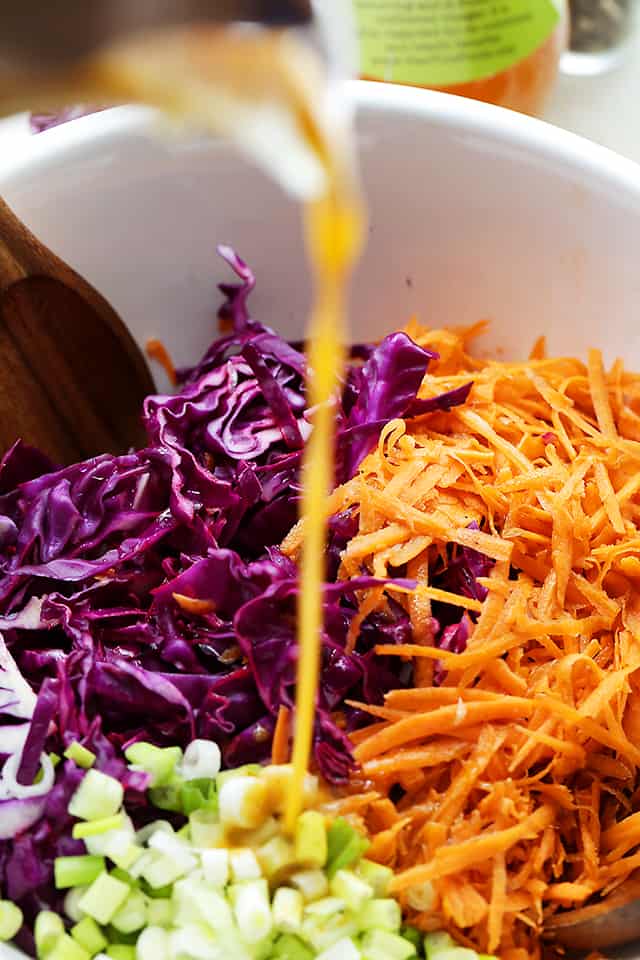 Pouring dressing over shredded red cabbage, carrots, and sliced green onions.