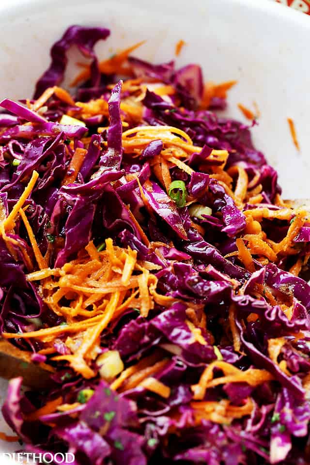 Close up of red cabbage slaw with shredded carrots and green onions in a bowl.
