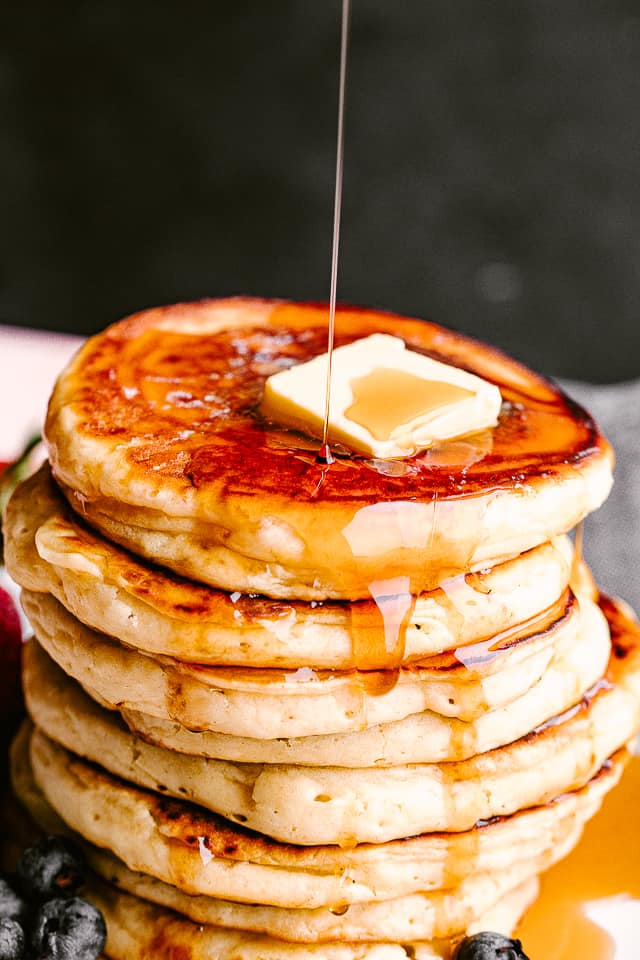 Pouring syrup over a stack of pancakes.