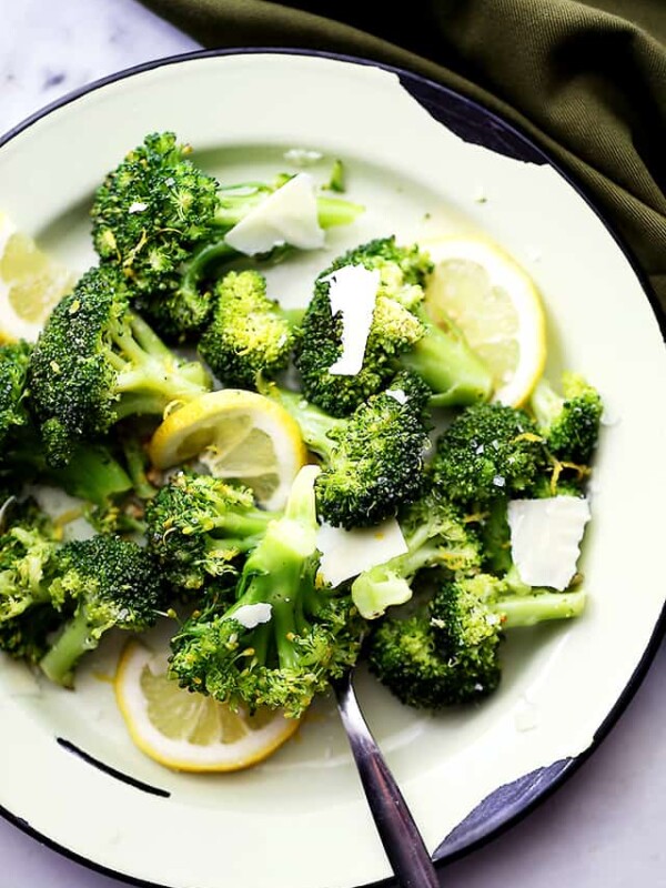 Plate of steamed broccoli with buttery breadcrumbs and lemon wedges.