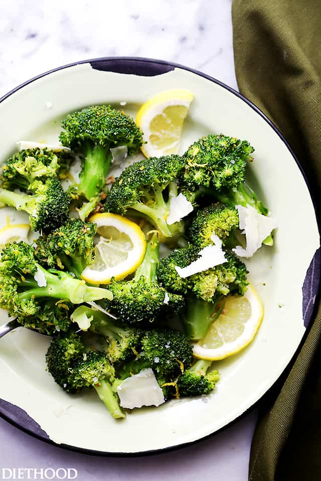 A plate of steamed broccoli topped with shavings of parmesan cheese.