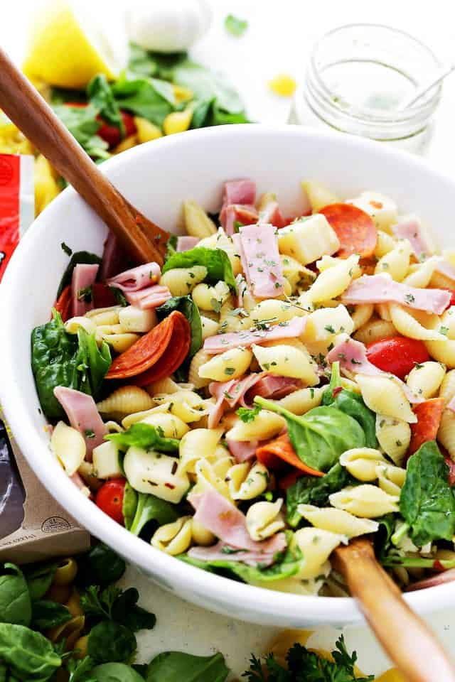 Italian pasta salad in a white bowl with two wooden salad spoons.