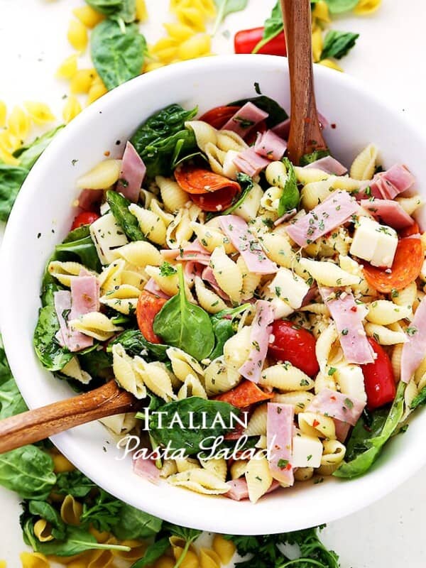 Overhead view of Italian pasta salad in a white bowl with two wooden salad spoons.