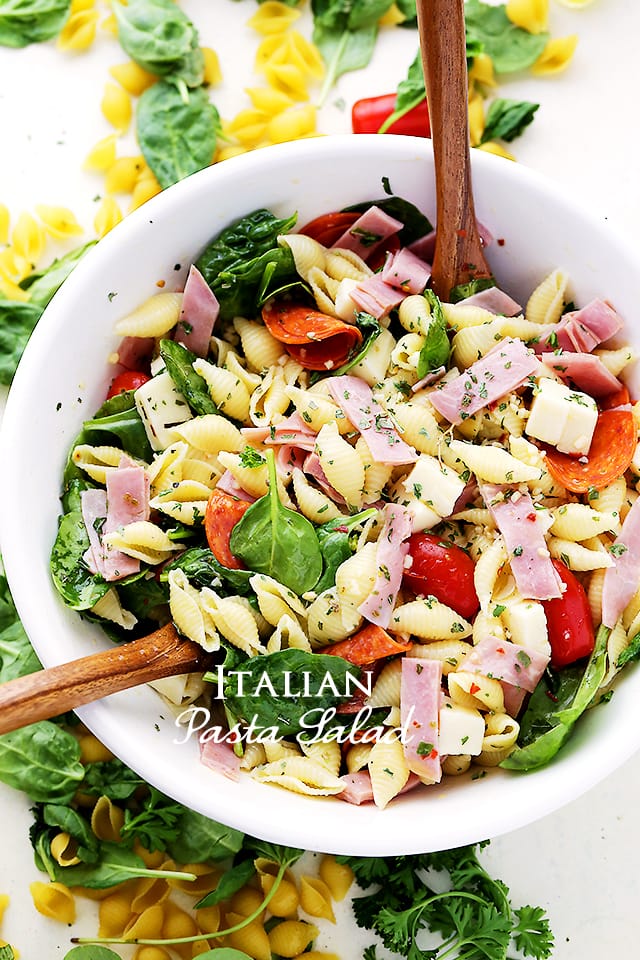 Overhead view of Italian pasta salad in a white bowl with two wooden salad spoons.