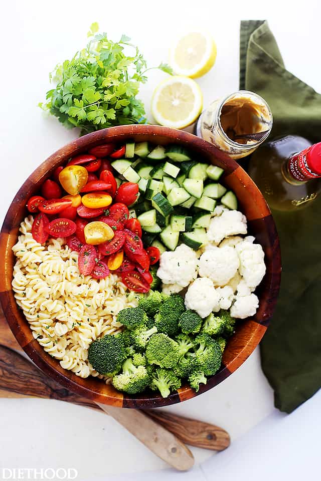 A large wooden bowl with pasta, tomatoes, broccoli, cauliflower and cucumbers 