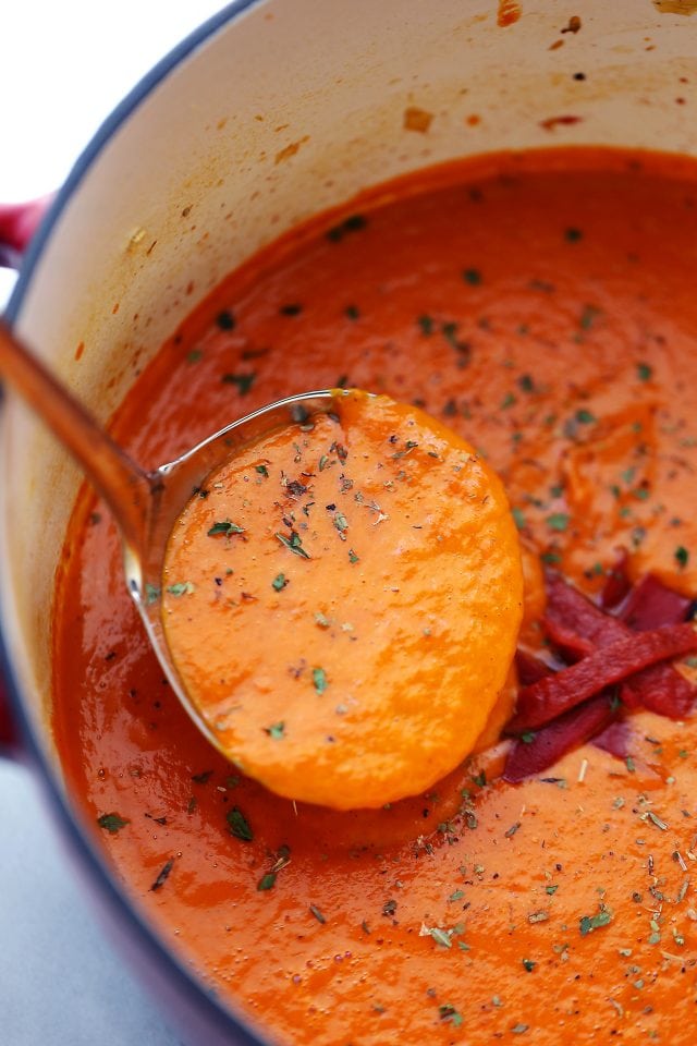 overhead shot of a ladle scooping out peppers tomato soup from a soup-pot.