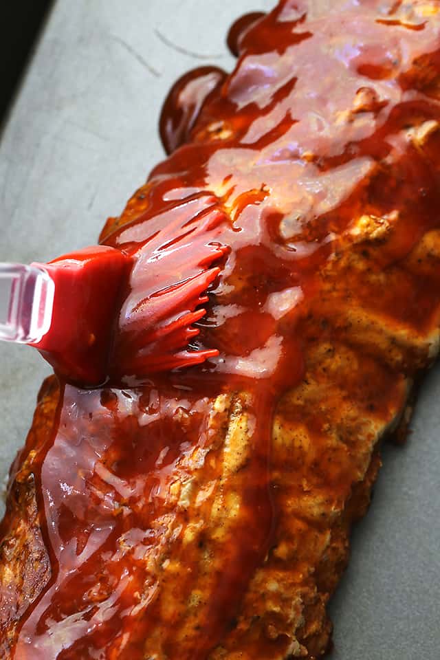 Barbecue Sauce Being Brushed Onto Smoky Pork Ribs Over a Gray Surface