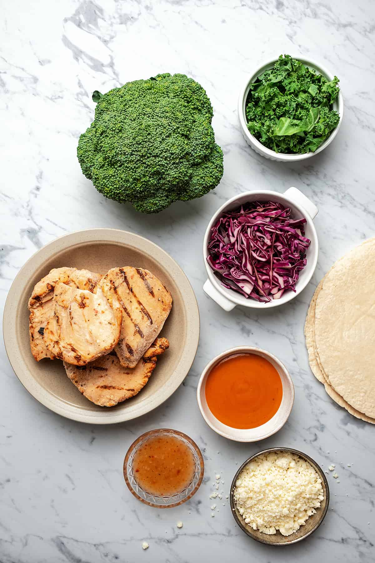 From top left: Fresh broccoli, chopped kale, red cabbage, frozen grilled chicken breast, buffalo sauce, Italian dressing, feta cheese, tortillas.