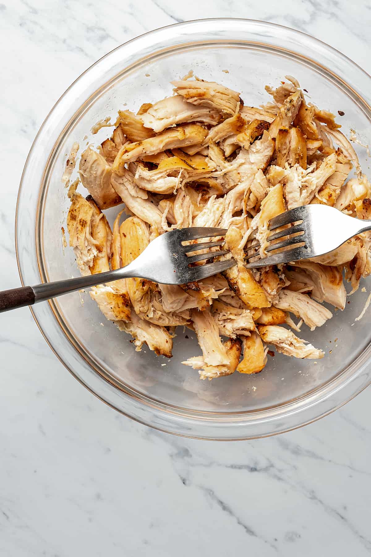 Chicken being shredded with two forks.