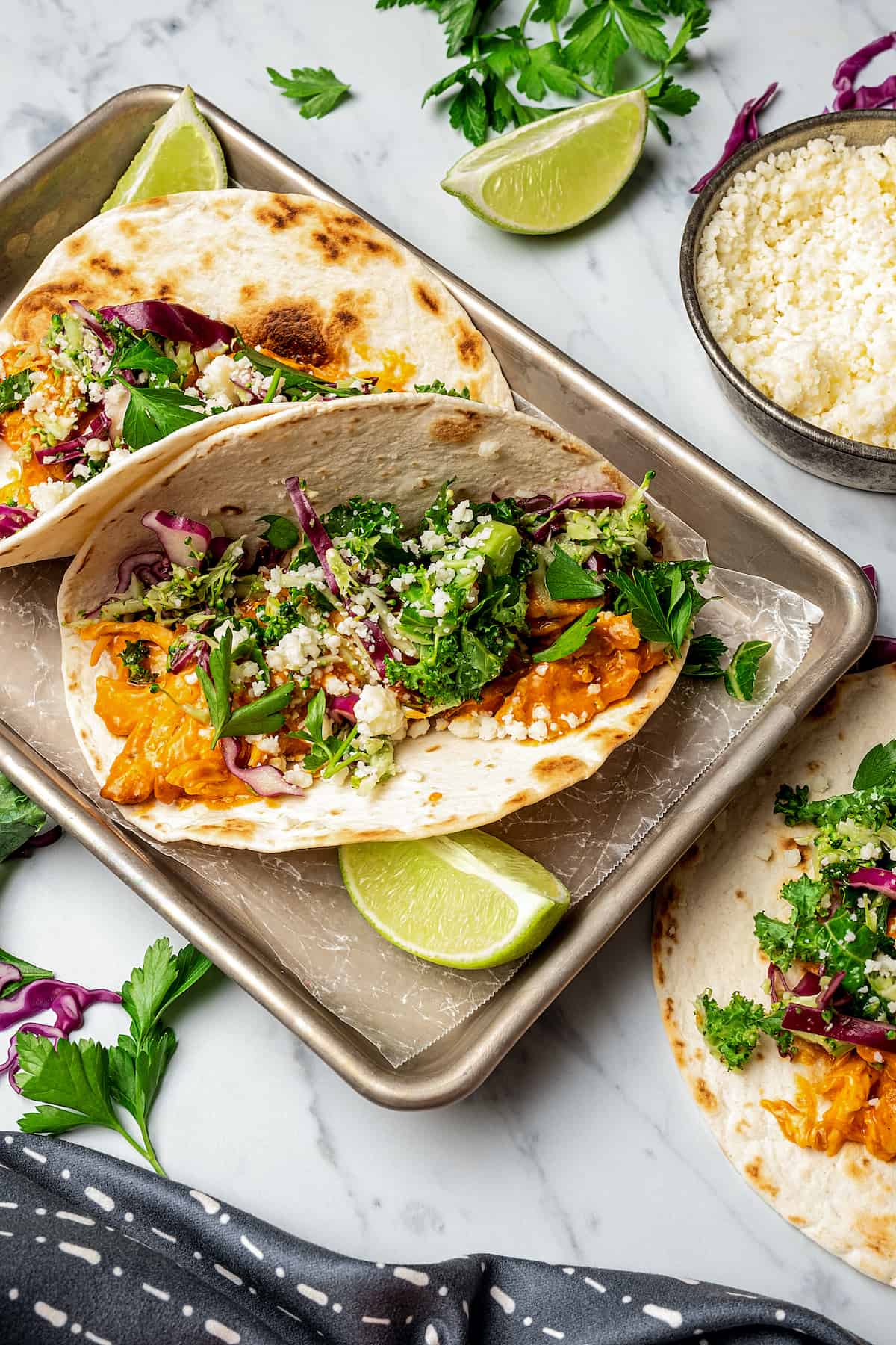 Shredded chicken tacos with buffalo sauce on a small baking tray, garnished with lime wedges.